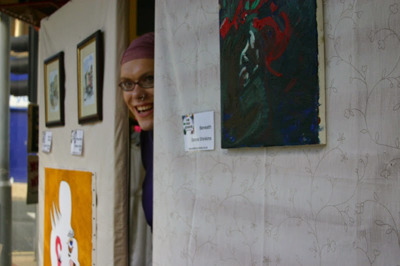 Picture of my friend Violet, a woman in glasses looks out from a row of artwork.