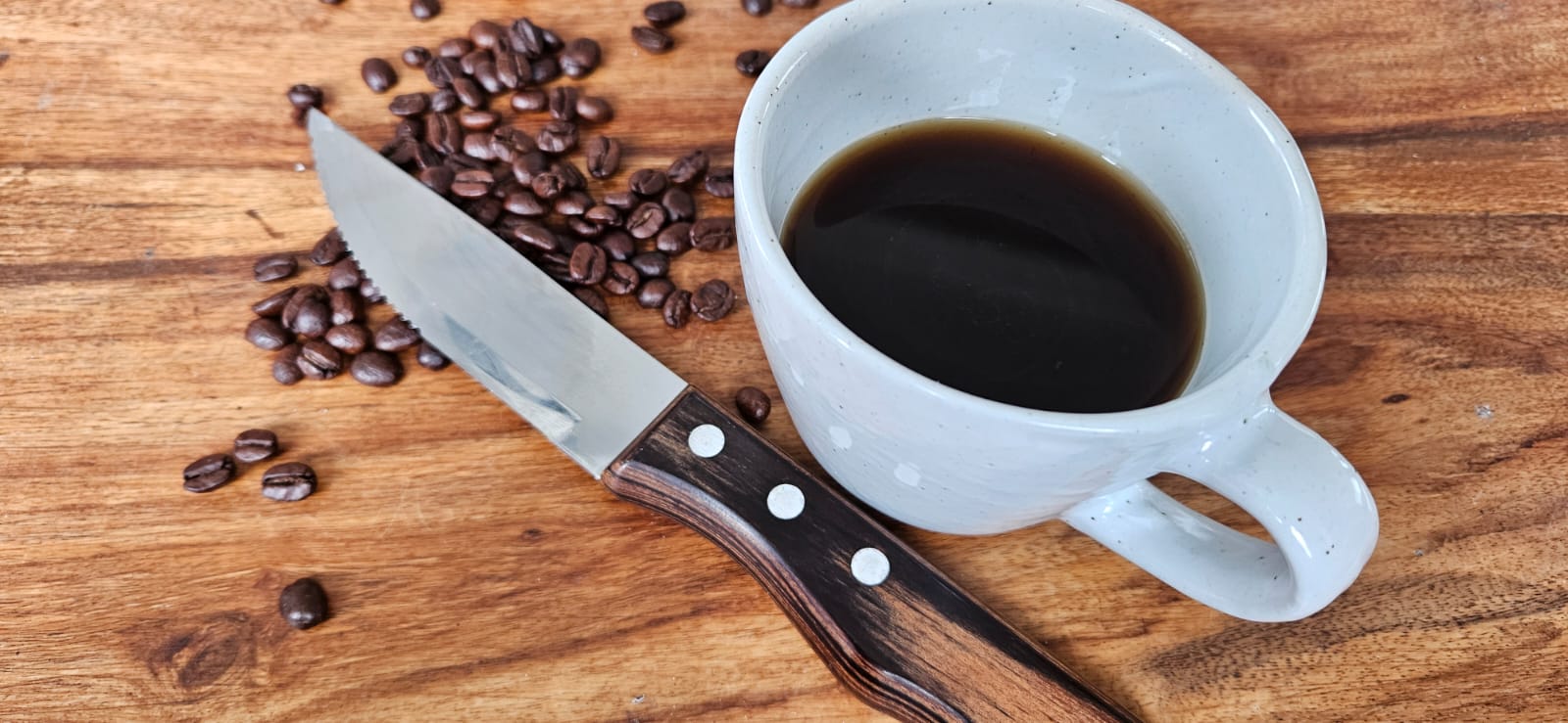 A mug of coffee, some coffee beans and a knife on a table